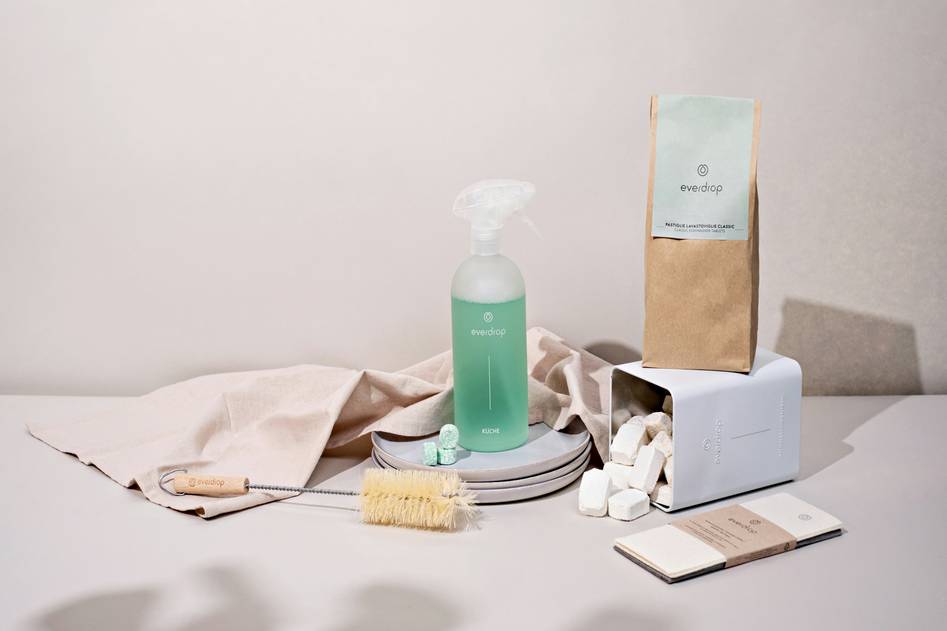 Bottle of biodegradable dish soap beside fresh herbs on wooden counter
